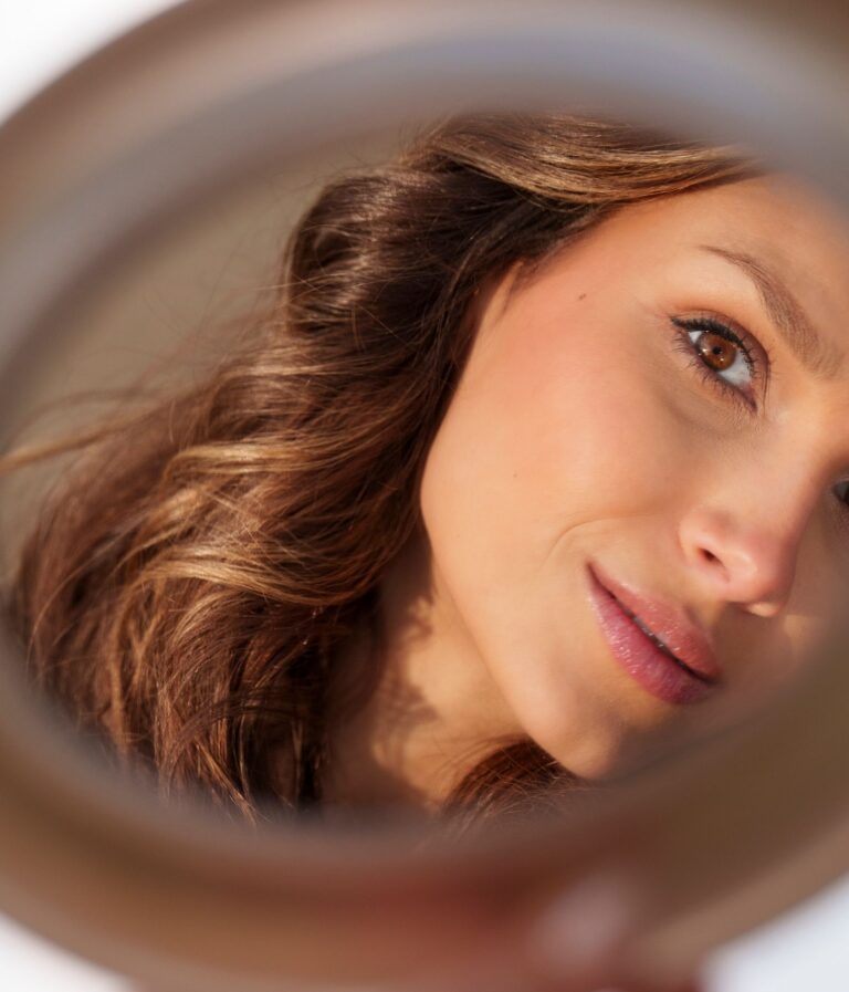 Close-up shot of a woman looking into a handheld mirror with natural lighting.