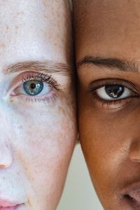 Crop female with freckles and blue eyes touching head with serious African American woman and looking at camera