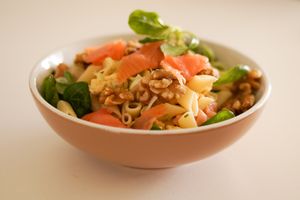 Delicious pasta salad featuring smoked salmon, walnuts, and fresh greens in a ceramic bowl.